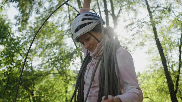 Climbing girl wraps rope around neck. Young woman in protective helmet wraps herself with climbing rope, preparing for mountaineering lesson. Importance of Compliance Safety in Extreme Sports.