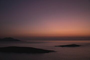 Sunset view from Monteferro's Rosa dos Ventos viewpoint, showcasing a serene horizon over tranquil seas. Silhouettes of Estelas Islands and distant Cabo Silleiro under a vibrant orange and purple sky.