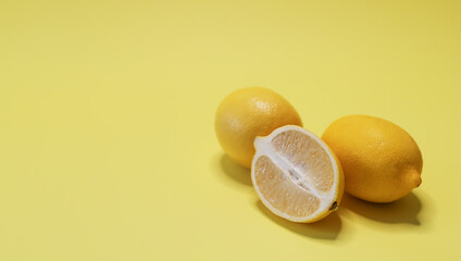 Two whole lemons on yellow background. Citrus fruit sliced in half. Copy space