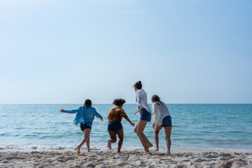 Group of young friends joyfully running into the sea, splashing water around in the sunshine.