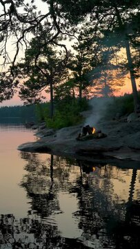 A bonfire burning in a forest on the shore of a lake at midnight on the Summer Solstice. Summer White Night on the eve of Midsummer Day in Finland. Sound of campfire and wildlife, birdsong