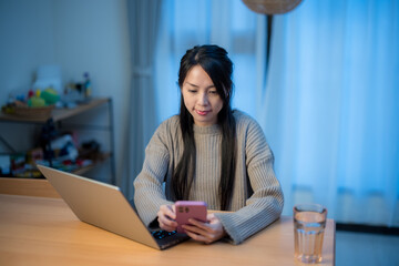 Woman work on laptop computer with mobile phone at home