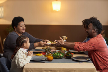Side view portrait of three generation African American family enjoying dinner together in cozy...