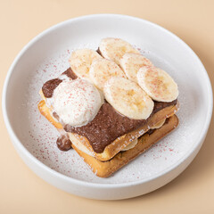 Belgian waffles with banana and chocolate sauce on a beige background