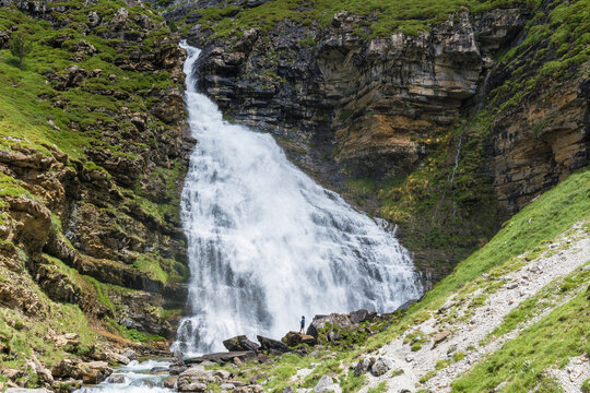 A hiker stands by a roaring waterfall in the Ordesa Valley, showcasing the scale and beauty of the Parque Nacional de Ordesa y Monte Perdido