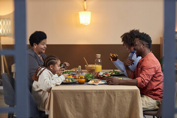Fototapeta na wymiar Side view portrait of three generation African American family eating dinner together at table in cozy home shot through open doors