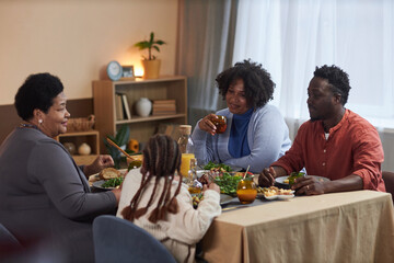 Three generation African American family eating dinner together at table in cozy home and enjoying conversation