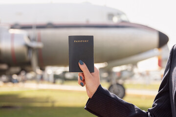 Anonymous air hostess's hand is displayed holding up a passport with a vintage airplane in the soft-focused background, symbolizing travel readiness
