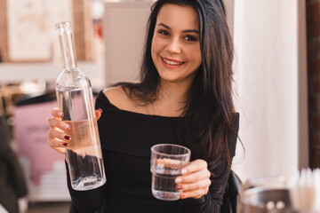Woman pours water into a glass from a glass bottle. Brunette woman have a good time in cafe, she...