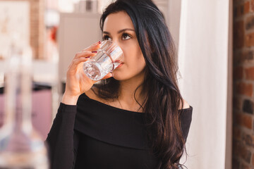 Delighted girl sitting in the cafe hold and drink glass of water. Food, leisure and people concept. Brunette hair woman wear black long sleeves top.  