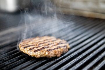 A sizzling burger patty cooks on a grill, smoke rising from its appetizing grill marks