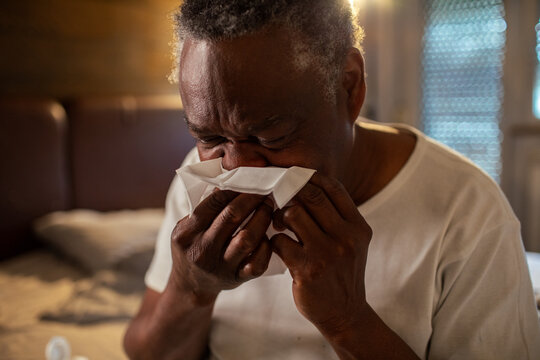 Senior man blowing nose in paper tissue in bedroom
