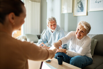 Elderly couple greeting a visitor at home with a handshake and smiling