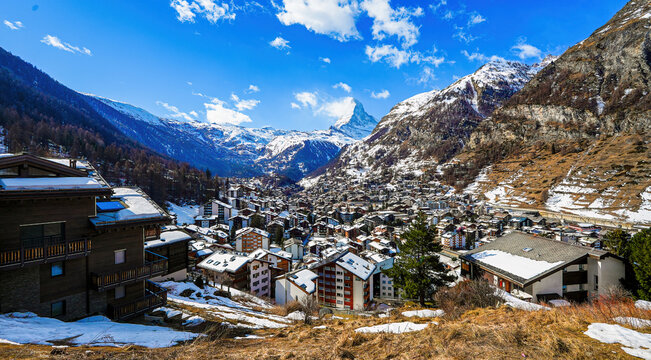 Aerial view of the village of Zermatt overlooked by the Matterhorn peak in the Swiss Alps in winter - Idyllic landscape with wooden chalets surrounded by snow capped mountains