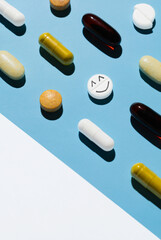 many different pills on a blue background with a white area and a pill with a smiley face. Preparation on the subject of medicine and health
