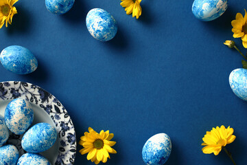Happy Easter greeting card. Easter eggs on plate and yellow flowers on dark blue background.