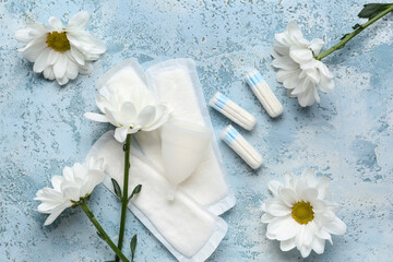 Composition with menstrual pads, cup, tampons and chamomile flowers on color background