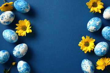 Happy Easter greeting card. Blue Easter eggs with yellow flowers on dark blue background. Flat lay, top view, copy space.