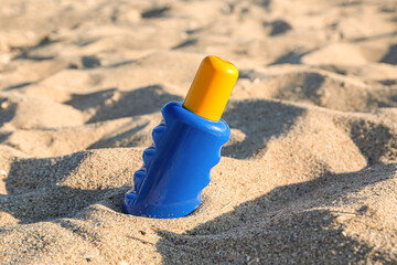 Bottle of sunscreen cream on sand at sea beach