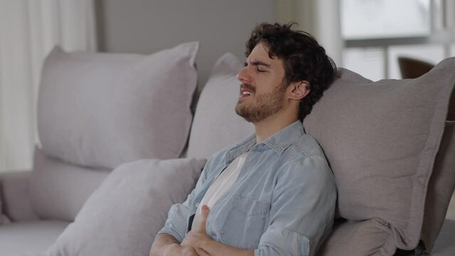 Young caucasian man lying on sofa feeling sudden strong abdominal stomach ache, gastritis problem. White guy having symptom poisoning diarrhea indigestion peptic ulcer pancreatitis at home apartment r