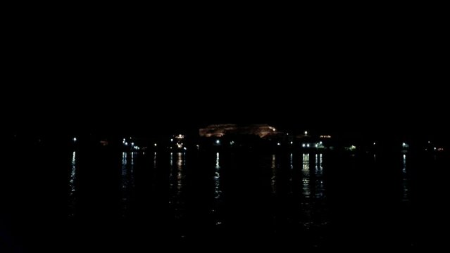 July 7, 2021 - Nile River, Luxor Egypt. The dark water reflects the illuminated mountain and buildings on the West Bank of Luxor as the small boat crosses the Nile River.