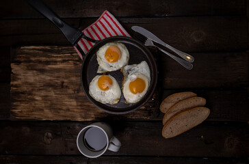 Fried eggs in a pan with vegetables and herbs on a black background.