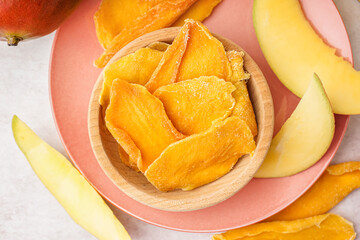 Wooden bowl with slices of dried mango on white table