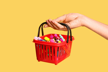 Female hand with shopping basket and different school markers on beige background
