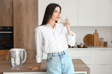 Young woman drinking filtered water in kitchen