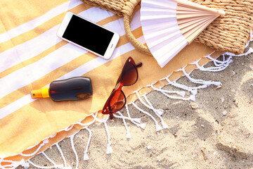 Stylish sunglasses with phone and beach accessories on sandy background