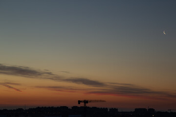 Sunrise over the city with the moon and crane against the background of the colorful sky