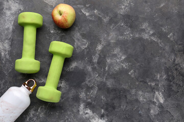 Dumbbells, bottle for water and apple on black background