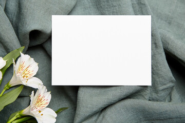 A landscape-oriented blank white card presented on a crinkled teal cloth, with fresh alstroemeria...
