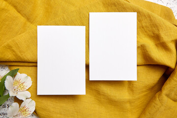 Two blank invitation cards on a rich golden textile background, accompanied by white alstroemeria flowers