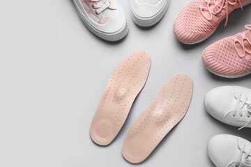 Pair of orthopedic insoles and stylish female shoes on grey background