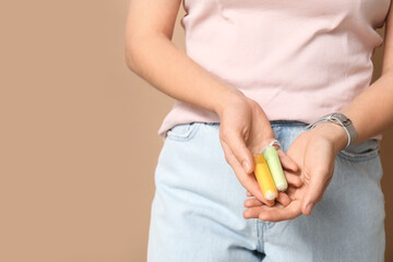Young woman with tampons on beige background, closeup