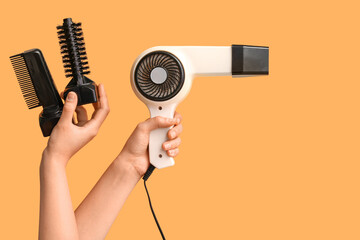 Female hands with hair dryer attachments on orange background.