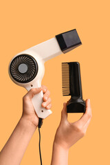 Female hands with hair dryer attachments on orange background.