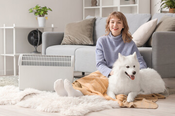 Young woman with plaid and Samoyed dog warming near radiator on floor at home