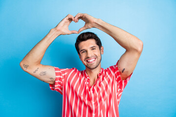 Photo of handsome appreciative man with bristle dressed striped shirt showing heart symbol over head isolated on blue color background