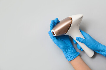 Female hands in rubber gloves with modern photoepilator on grey background, closeup