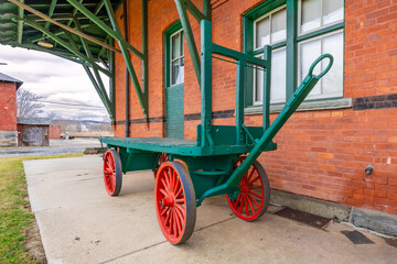 Vintage green wooden railway luggage cart with four wagon wheels along side a brick building.