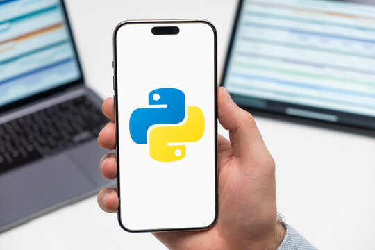 PRAGUE, CZECH REPUBLIC - JANUARY 21 2024: Python logo on the screen of smartphone in mans hand on the workplace background. 