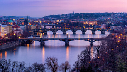 Fototapeta na wymiar Glowing twilight over Prague, with illuminated bridges arching over a peaceful river, surrounded by classical architecture and tree silhouettes