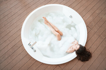 Overhead view of serene woman relaxing in bubble bath with foam.