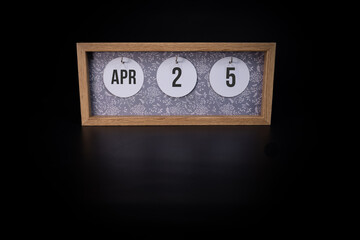 A wooden calendar block showing the date April 25th on a dark black background, save the date or date of an event concept.
