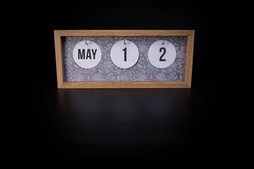 A wooden calendar block showing the date May 12th on a dark black background, save the date or date of an event concept.