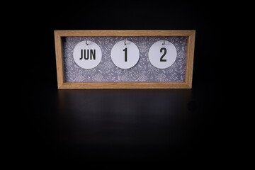 A wooden calendar block showing the date June 12th on a dark black background, save the date or date of event concept