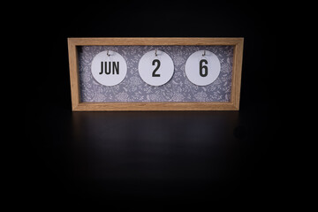 A wooden calendar block showing the date June 26th on a dark black background, save the date or date of event concept