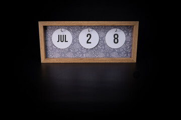 A wooden calendar block showing the date July 28th on a dark black background, save the date or date of event concept